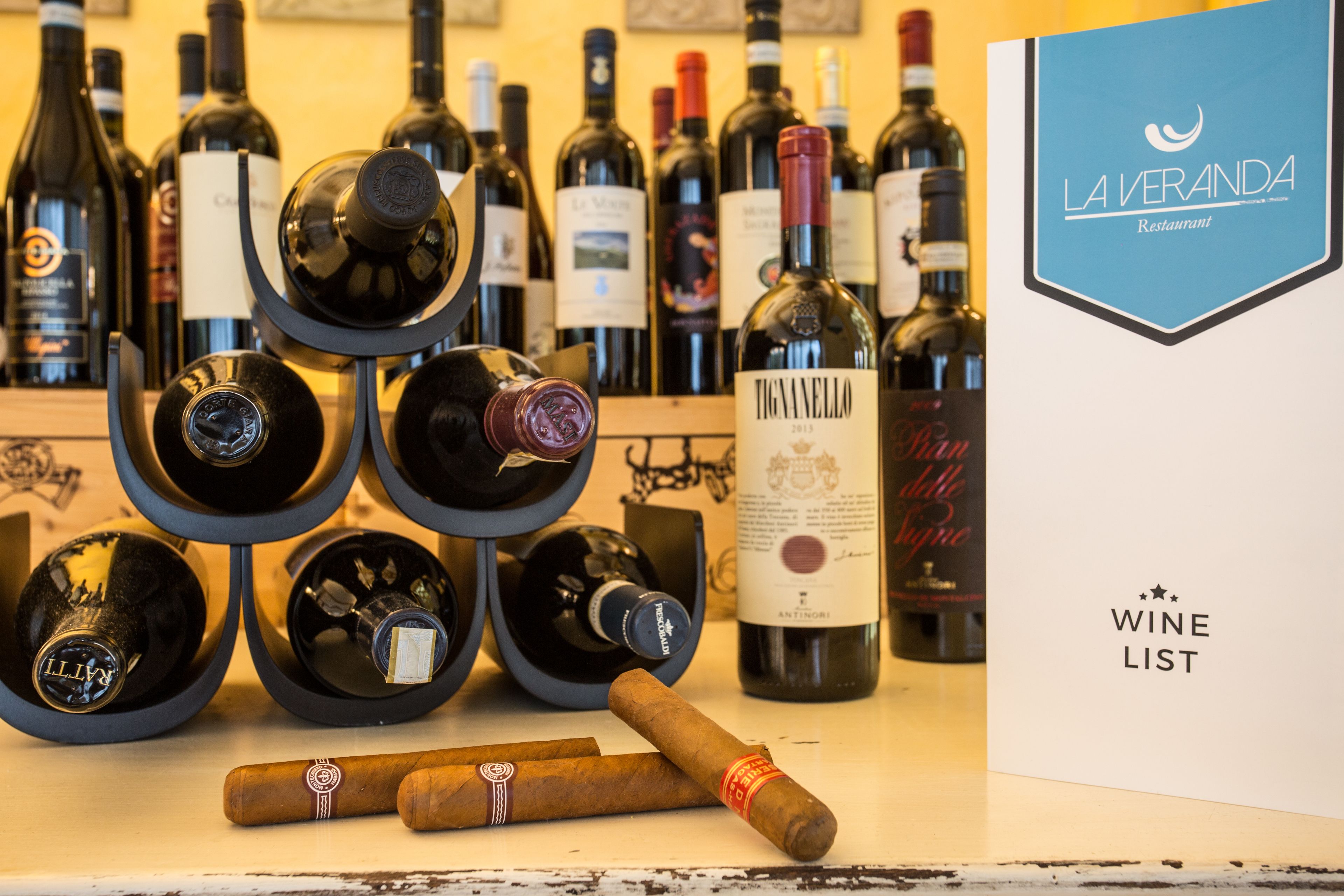 Uma adega com garrafas e charutos, um letreiro com a carta de vinhos, e um letreiro de restaurante.