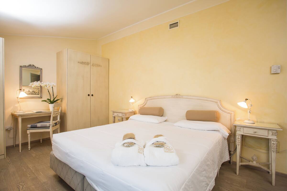 Camera d'albergo con un letto grande, due comodini, una scrivania con una sedia, un armadio e uno specchio.