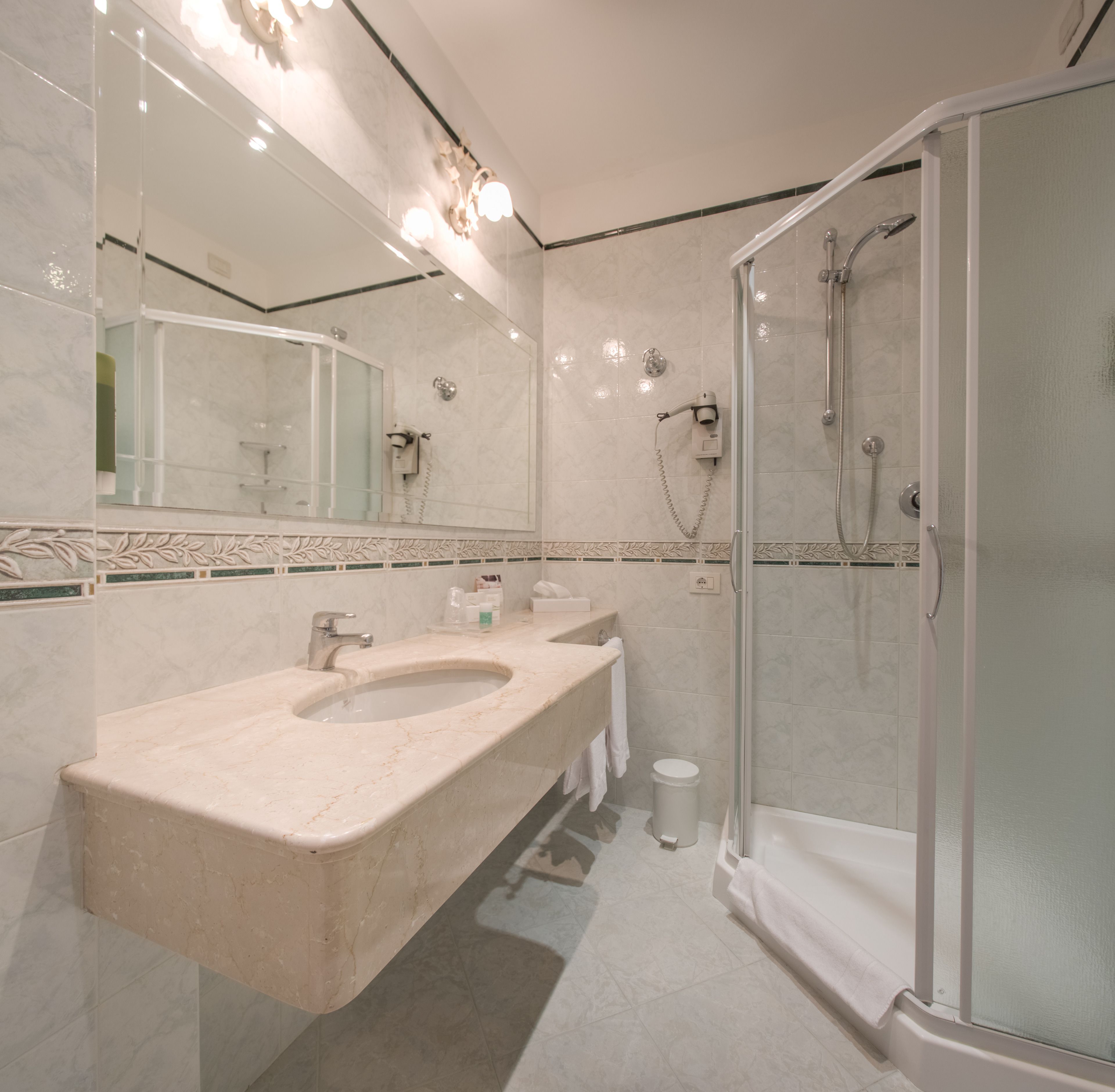 Une salle de bain moderne avec un grand miroir, deux lavabos, une douche et un espace douche fermé par des parois de verre.