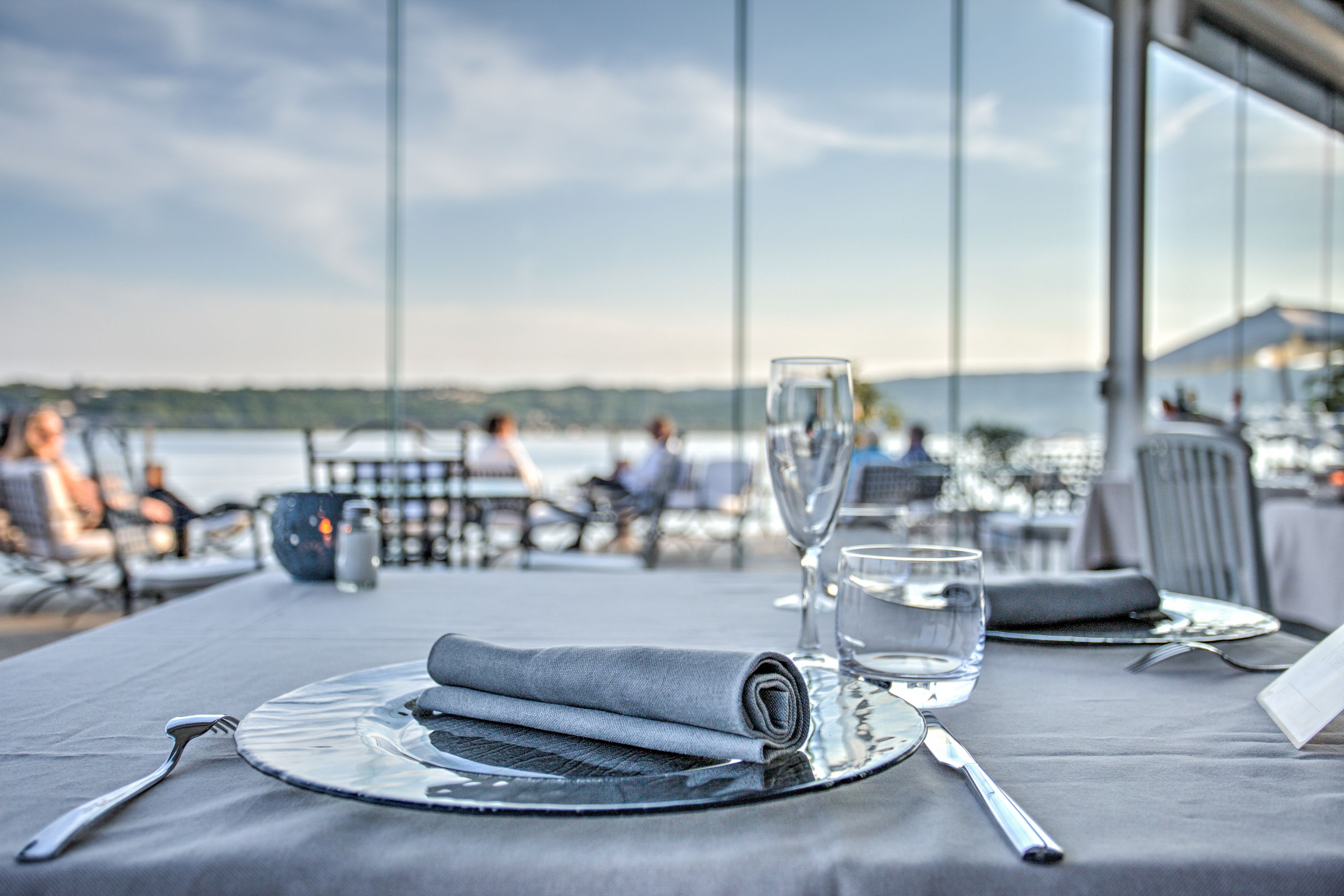 Une table dressée pour le dîner, avec vue sur la mer et des personnes en arrière-plan.