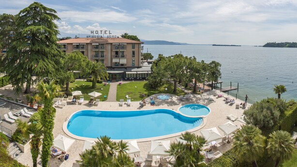 A hotel with a large swimming pool, lounge chairs, and a view of the sea. - Hotel Spiaggia d'Oro - Charme & Boutique by Double Hospitality (Salò)