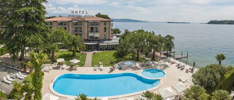 A hotel with a large swimming pool, lounge chairs, and a view of the sea.