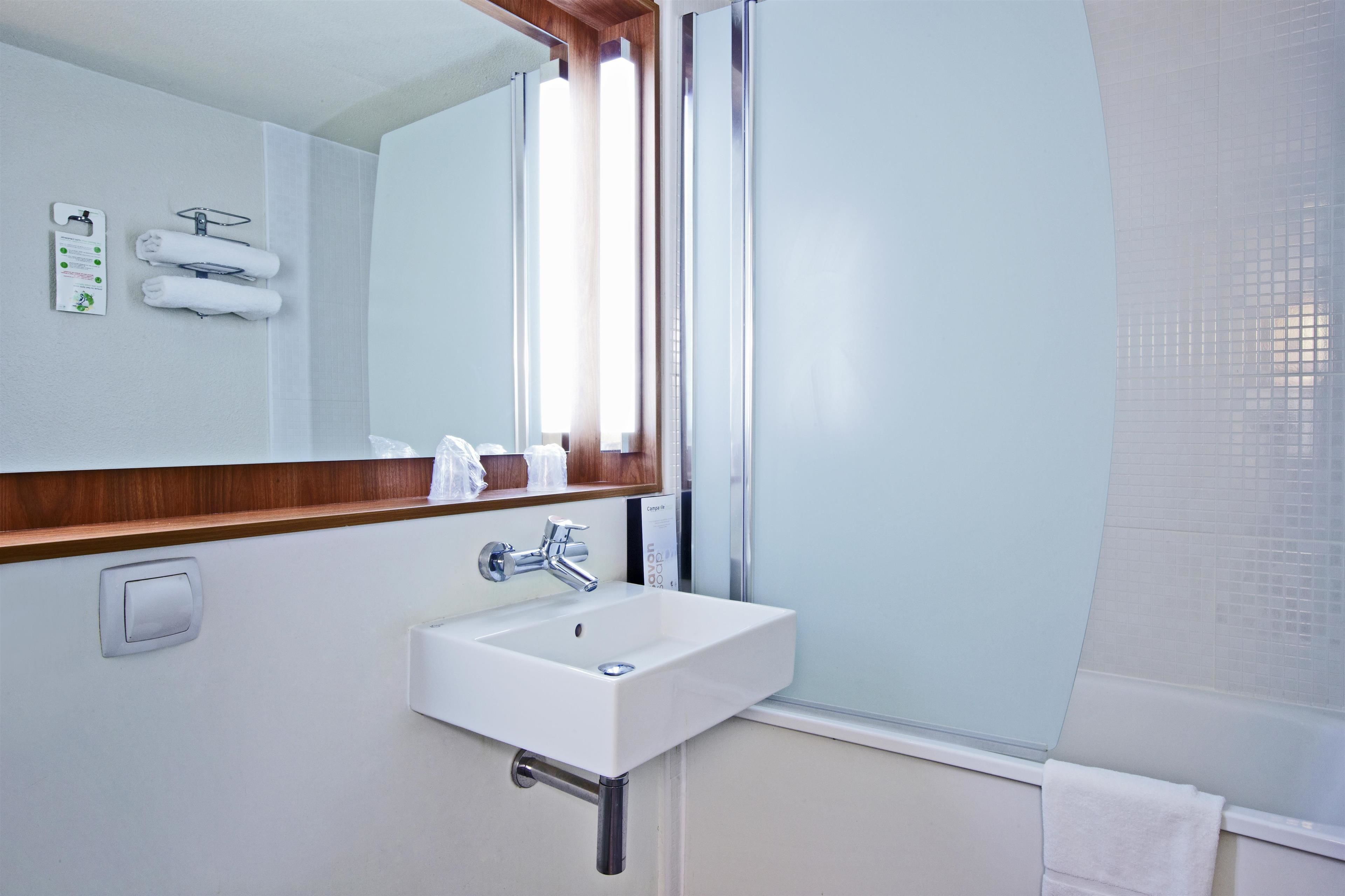 Un baño con lavamanos blanco, un espejo y una ventana.
