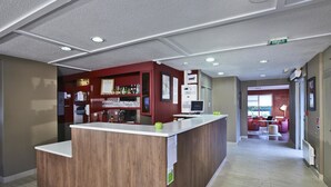 Un espace d’accueil avec un comptoir en bois, un bar avec des étagères remplies de bouteilles et un coin salon à l’arrière-plan.