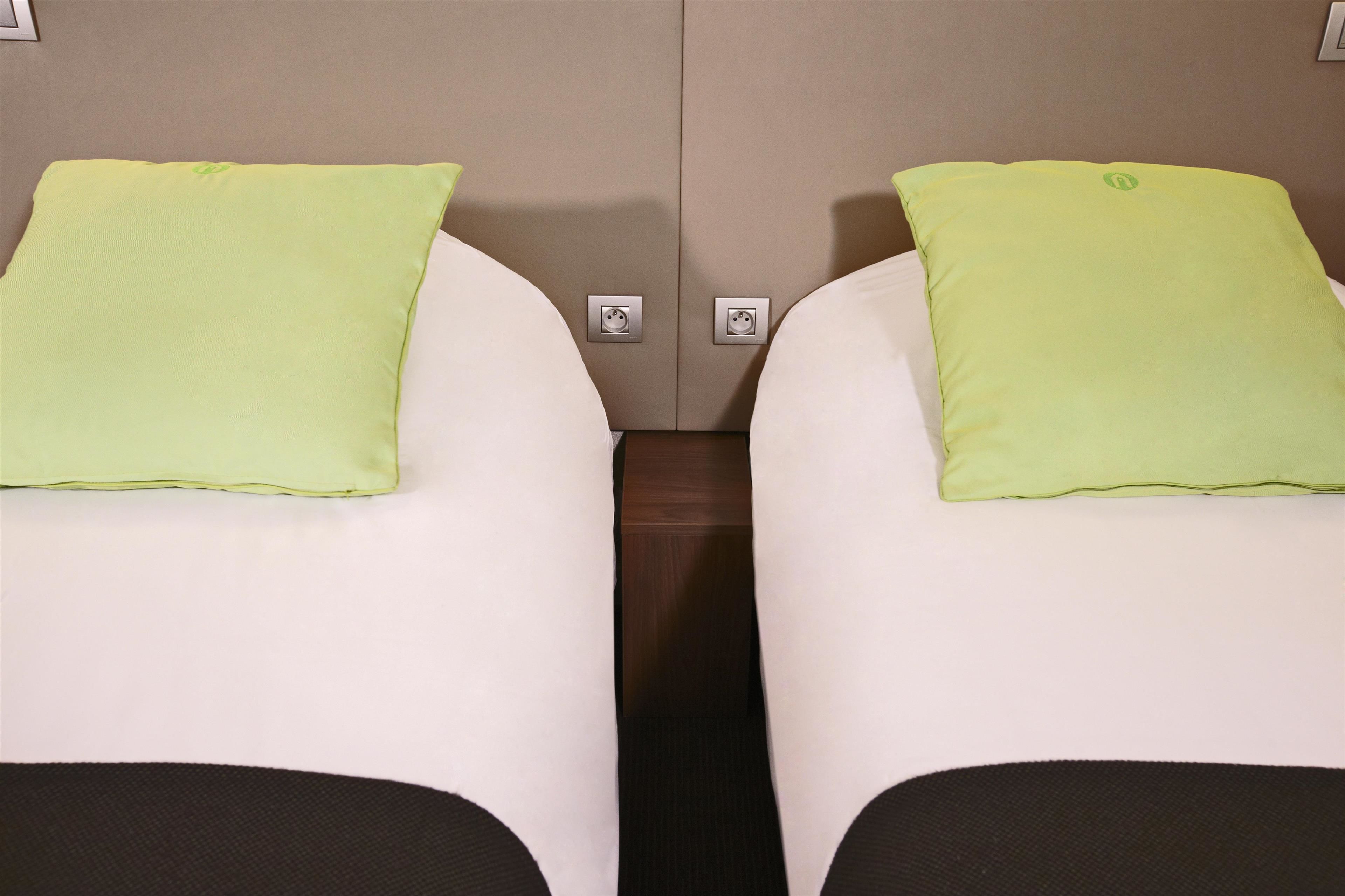 Two beds with green pillows and a wooden divider.