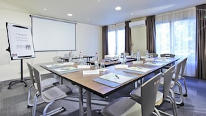 Une salle de conférence avec une longue table, des plaques nominatives, des chaises, un projecteur et un tableau blanc.