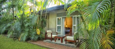 A tropical resort room with a bed, a small table, and two chairs.
