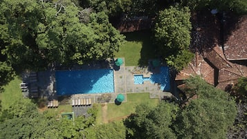 An aerial view of a swimming pool surrounded by lush greenery, with a tiled deck area and lounge chairs.