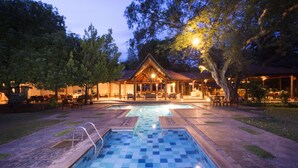 A pool area with a checkered pattern, a covered seating area, and a building with a sloped roof.