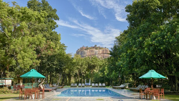 A pool area with lounge chairs and umbrellas, surrounded by trees and a view of a rocky cliff.