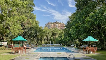 Relax by the serene pool surrounded by lush greenery and shaded by two umbrellas.