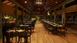 Un comedor interior amplio con mesas y sillas de madera, techos altos con vigas a la vista e iluminación ambiental.