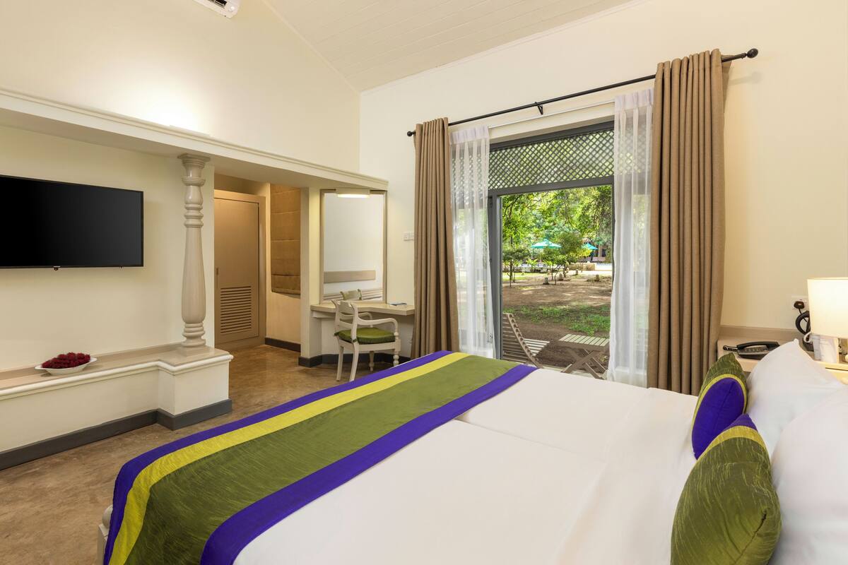 A hotel room with a bed, a desk, a chair, a TV mounted on the wall, and a view of the outdoors.