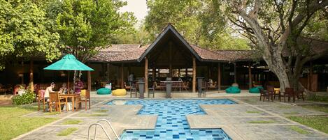 A pool area with a tiled deck, seating arrangements, and a covered pavilion.