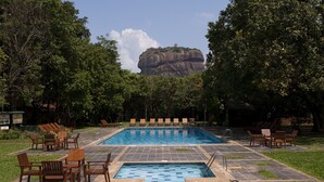A swimming pool with tiled flooring and wooden lounge chairs arranged around it.