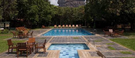 A swimming pool with tiled flooring and wooden lounge chairs arranged around it.