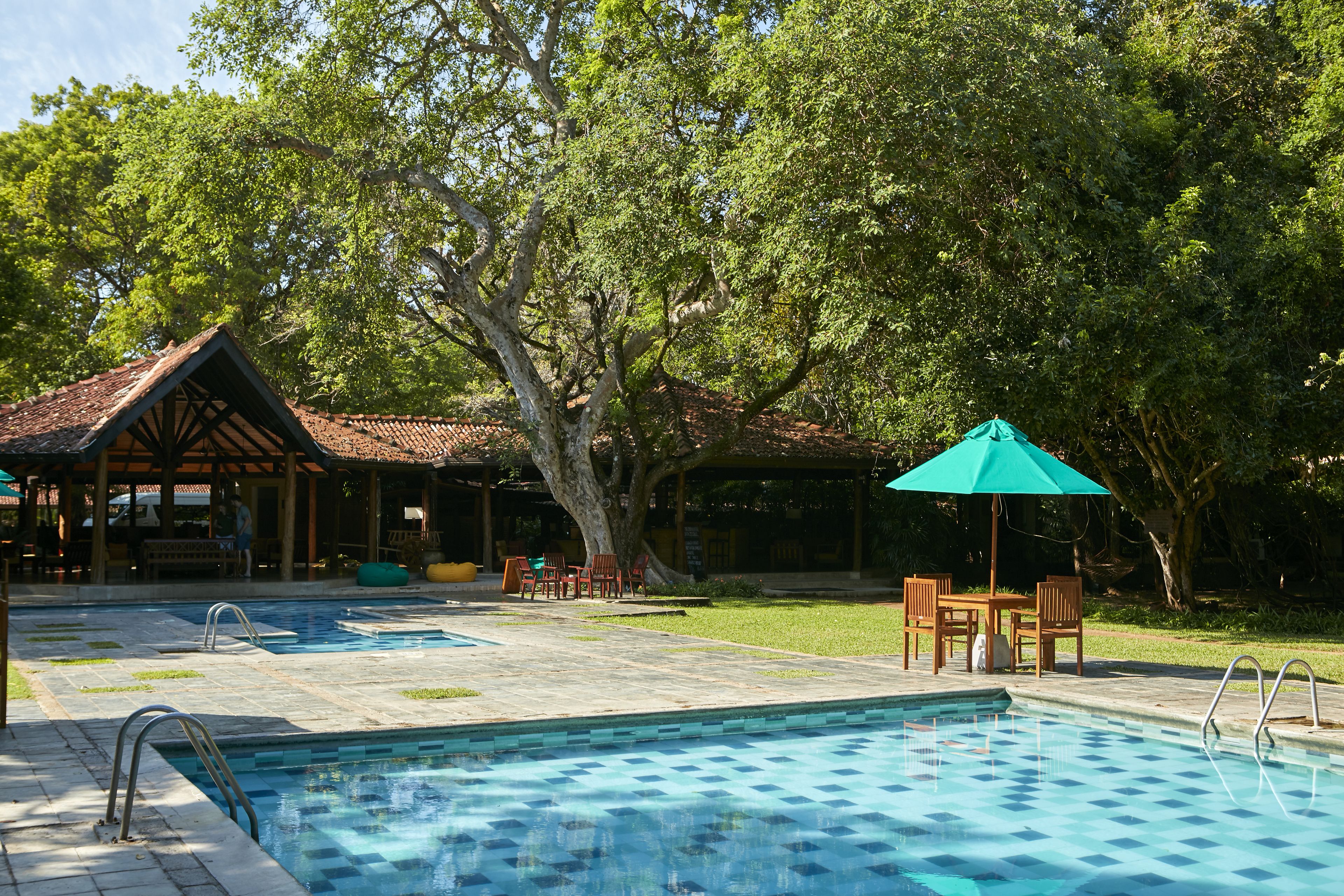 A swimming pool with a tiled deck, surrounded by trees and a gazebo with outdoor seating.