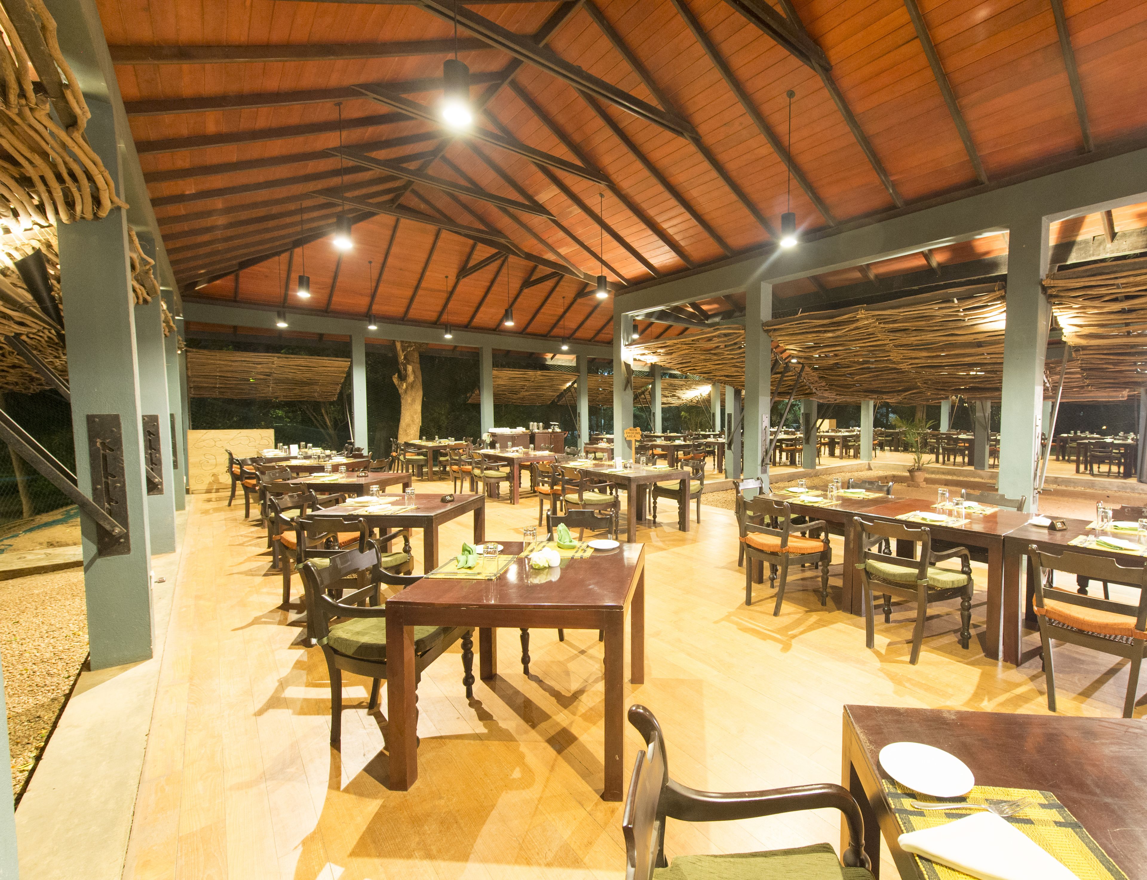 A spacious dining area with multiple tables and chairs, a high wooden ceiling, and a view of the outdoors.