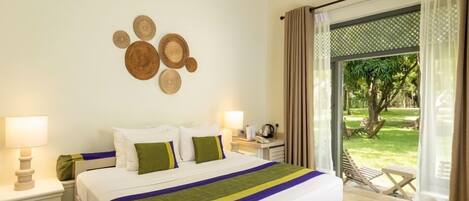 Habitación de hotel con cama, dos mesitas de noche, una lámpara, vista a un jardín a través de una puerta corrediza de vidrio y un adorno de círculos en la pared.