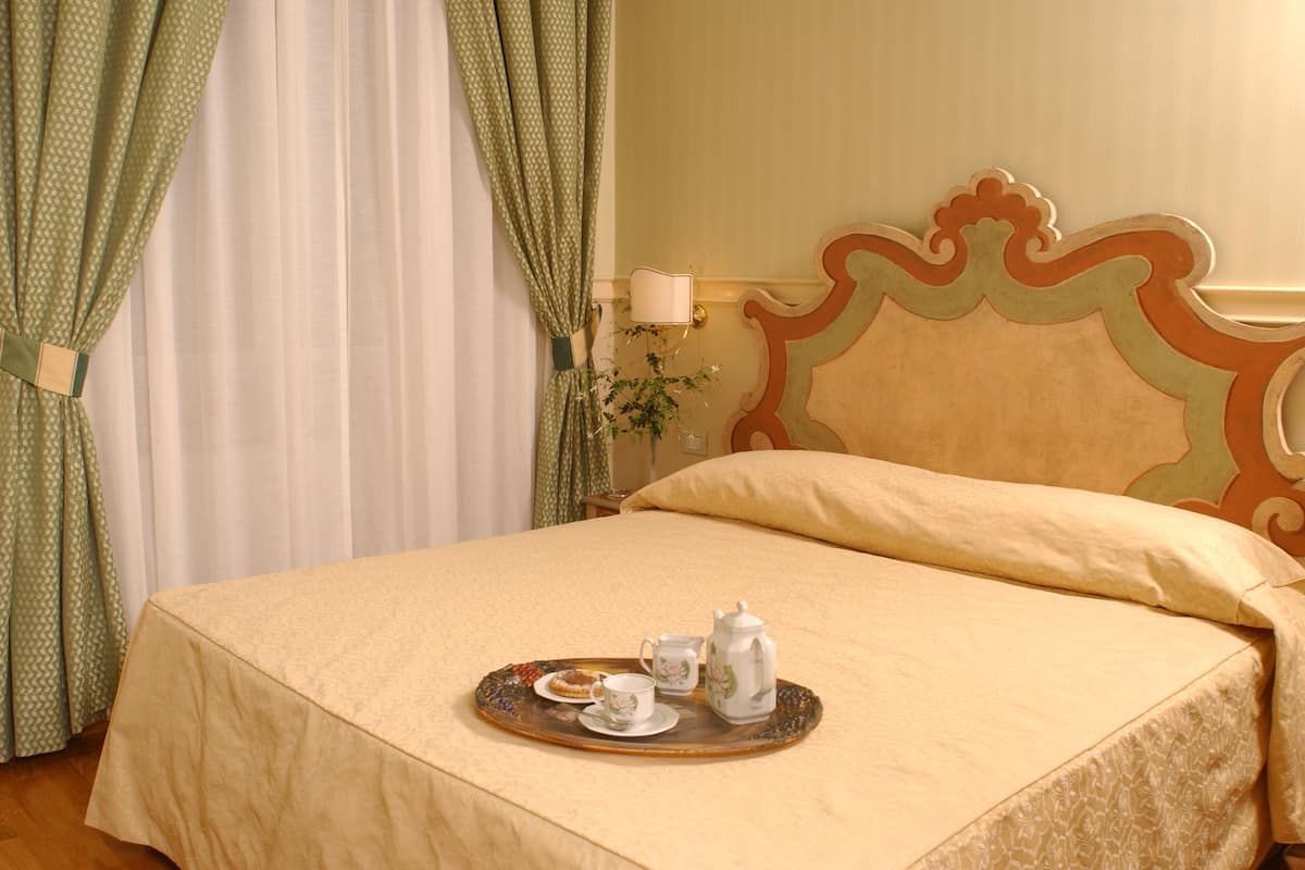 A neatly made bed with a tray of tea and pastries, a bedside lamp, and curtains.