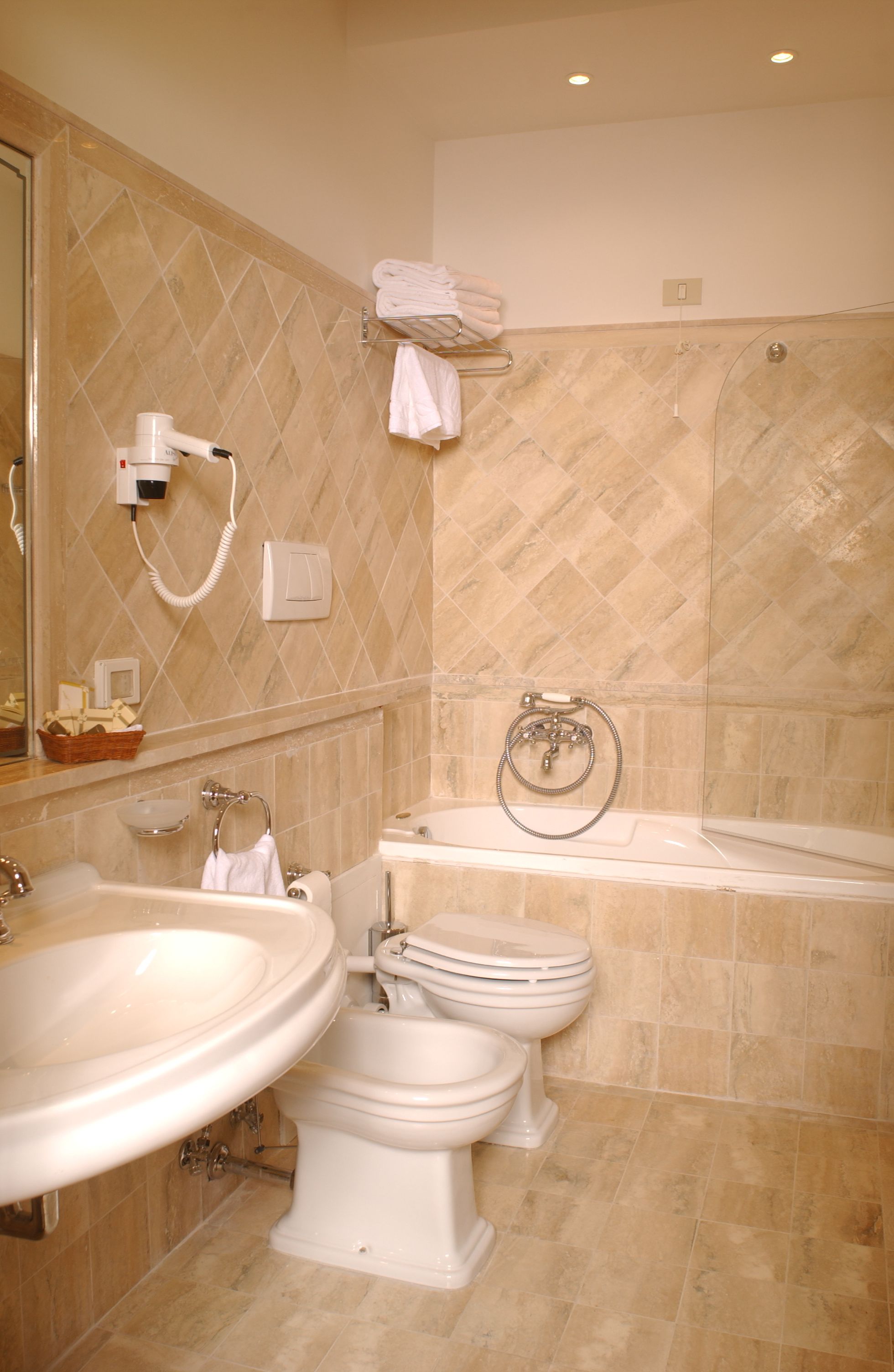 A bathroom with a large sink, two toilets, a bathtub, and a hairdryer on the wall.