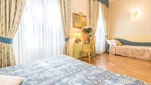 A hotel room with a large bed, a smaller bed, a desk with a lamp, a chair, and a painting on the wall. - Il Gattopardo Relais (Rome)