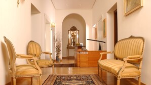 A hallway with two ornate chairs, a wooden desk, a mirror, and a patterned rug. - Il Gattopardo Relais (Rome)