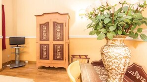 A room with a wooden cabinet, a television on a stand, a dining table with a chair, and a large vase with white flowers. - Il Gattopardo Relais (Rome)