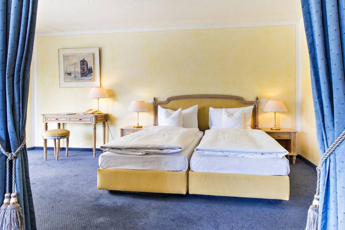 Een tweepersoonsbed met twee nachtkastjes, een bureau en een stoel in een kamer met een blauw tapijt en gele wanden.