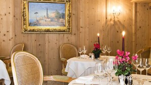 A dining room with a round table set for a meal, chairs, a painting on the wall, and a candelabra with candles. - Quadratscha Hotel (Samedan)