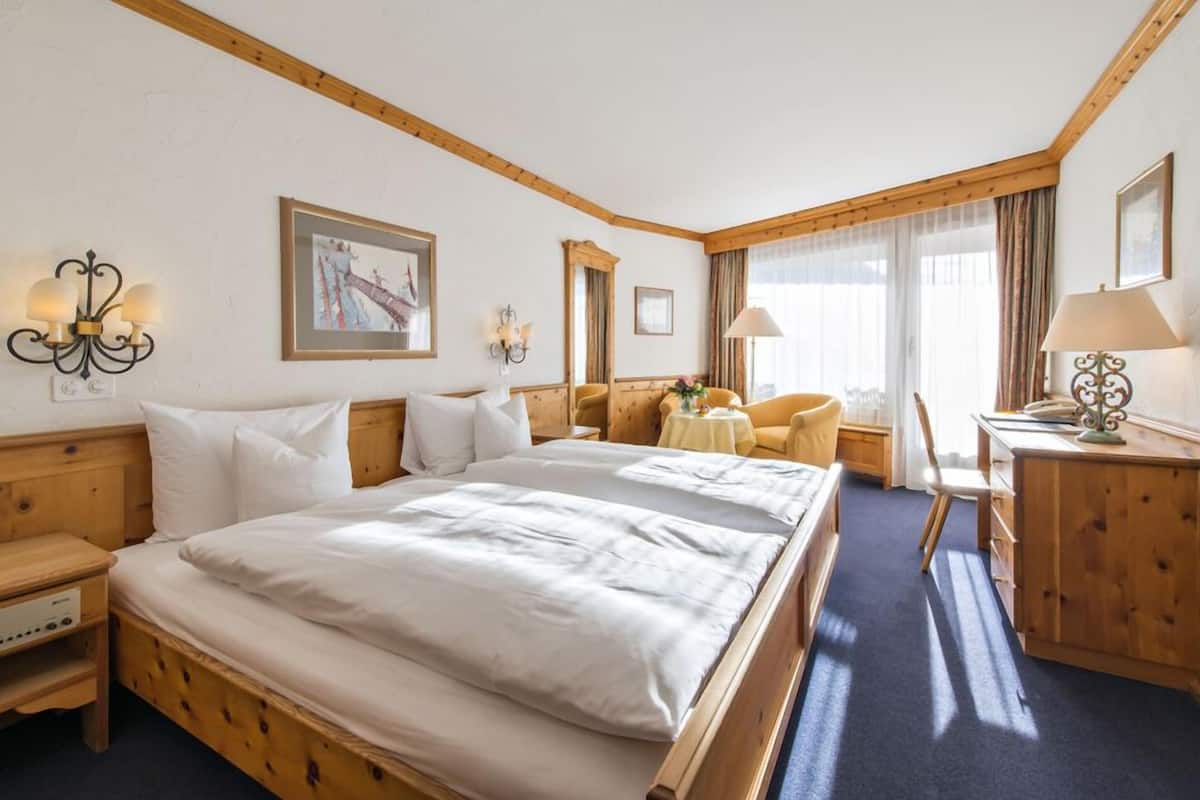 Een hotelkamer met een groot bed, een houten hoofdbord, twee nachtkastjes, een bureau met een lamp en een stoel.