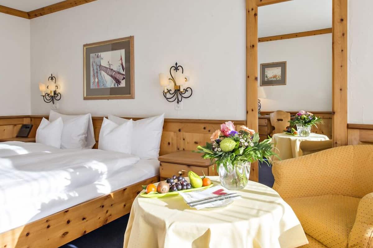 Een hotelkamer met twee bedden, een houten hoofdbord, een tafeltje met een bloemenvaas en een stoel.