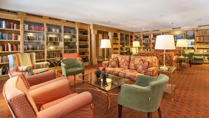 A library with bookshelves, a sofa, chairs, and lamps. - Quadratscha Hotel (Samedan)