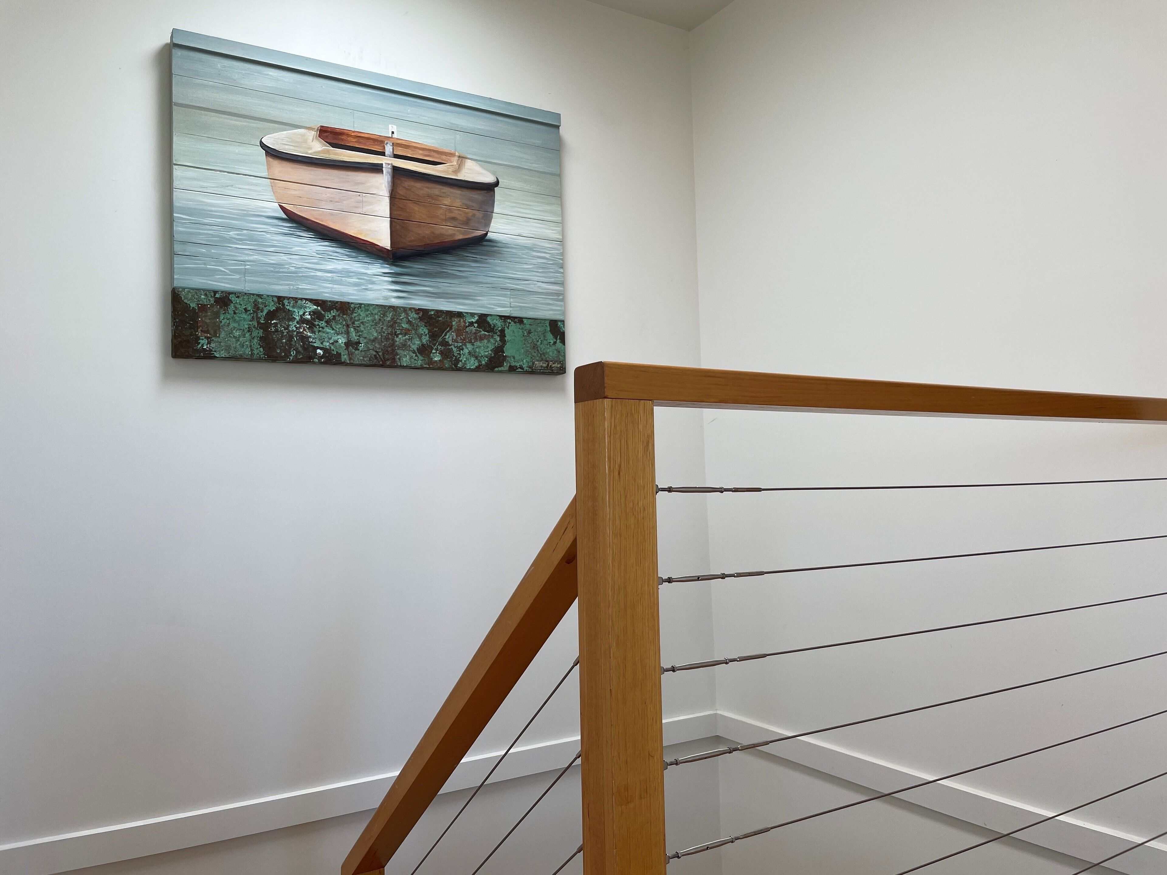 A staircase with a wooden handrail and metal balusters, leading to a landing with a wall-mounted painting of a boat.