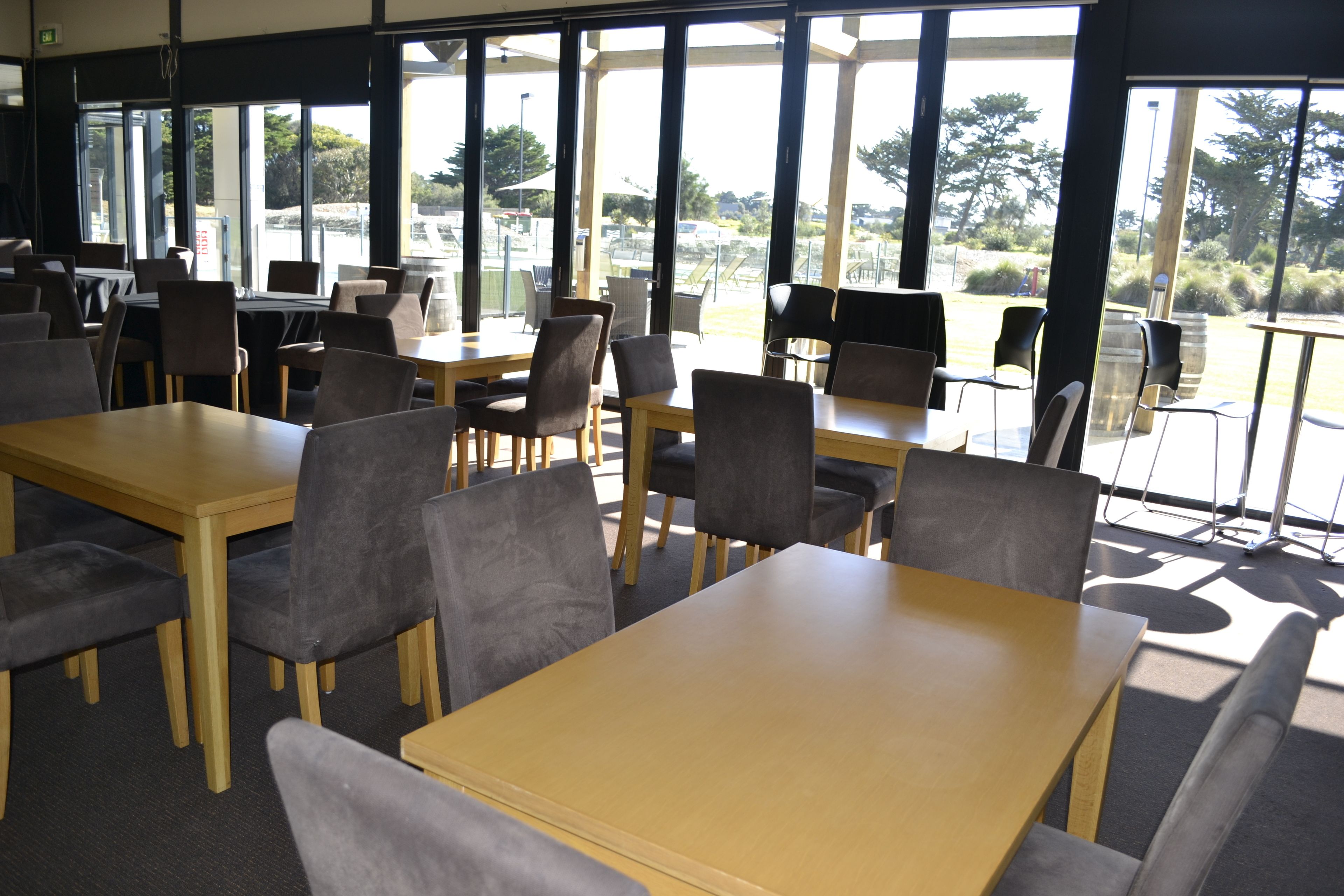 Un amplio comedor interior con varias mesas y sillas, y grandes ventanales que ofrecen vistas al exterior.