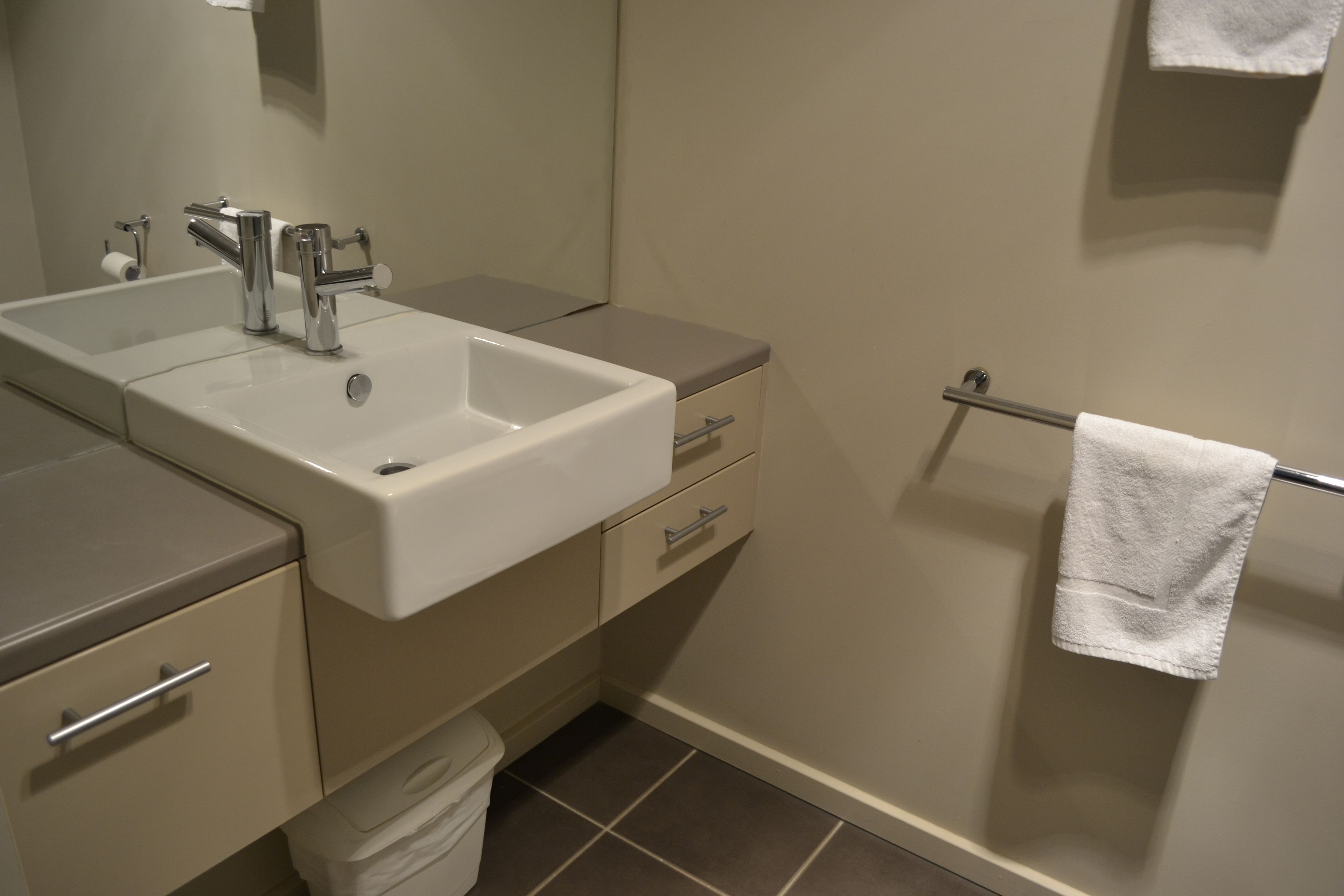 A bathroom with a double sink, a mirror, a towel rack, and a toilet.