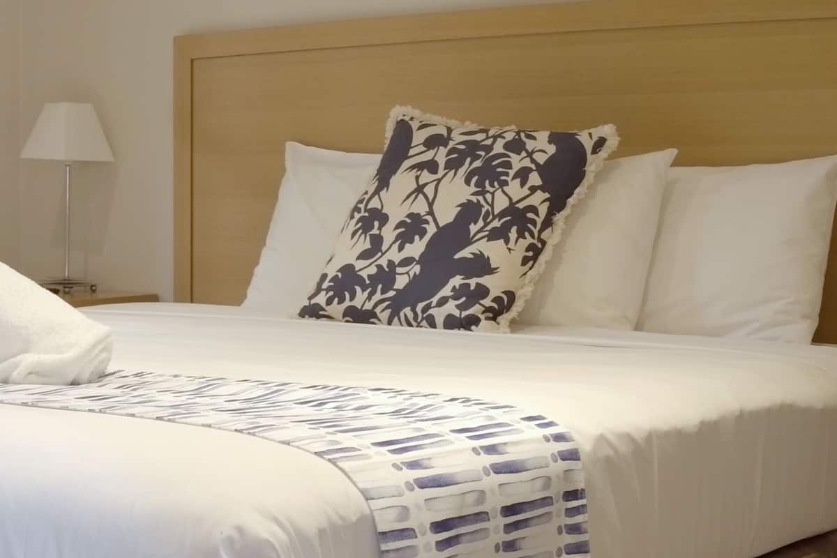A neatly made bed with a rolled white towel, a patterned pillow, and a white pillow.
