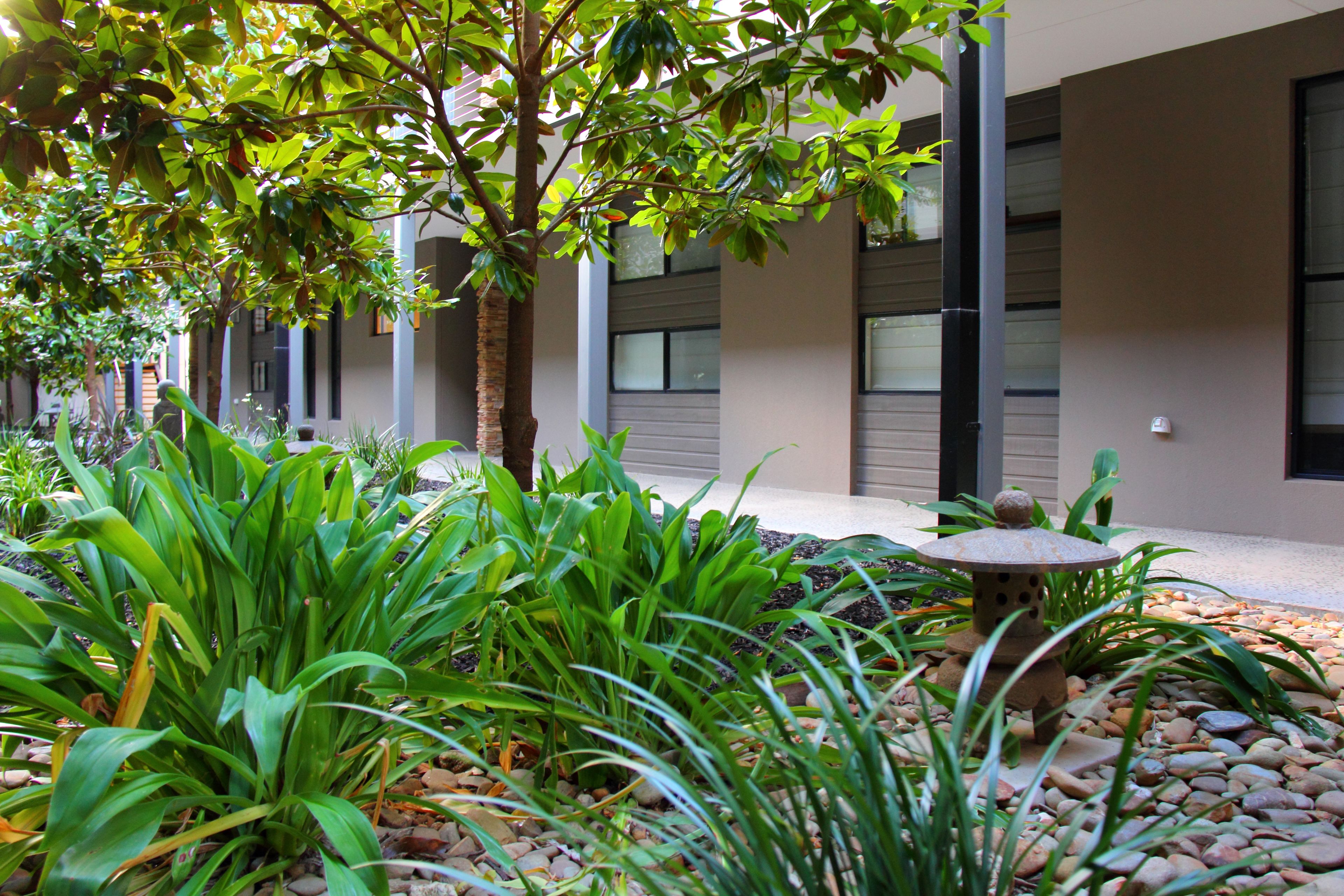 A courtyard with a stone lantern, green plants, and a building with large windows and a modern design.