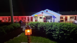 Um motel com um letreiro de neon indicando 'SEM QUARTO DISPONÍVEL' e uma máquina de refrigerantes Coca-Cola.