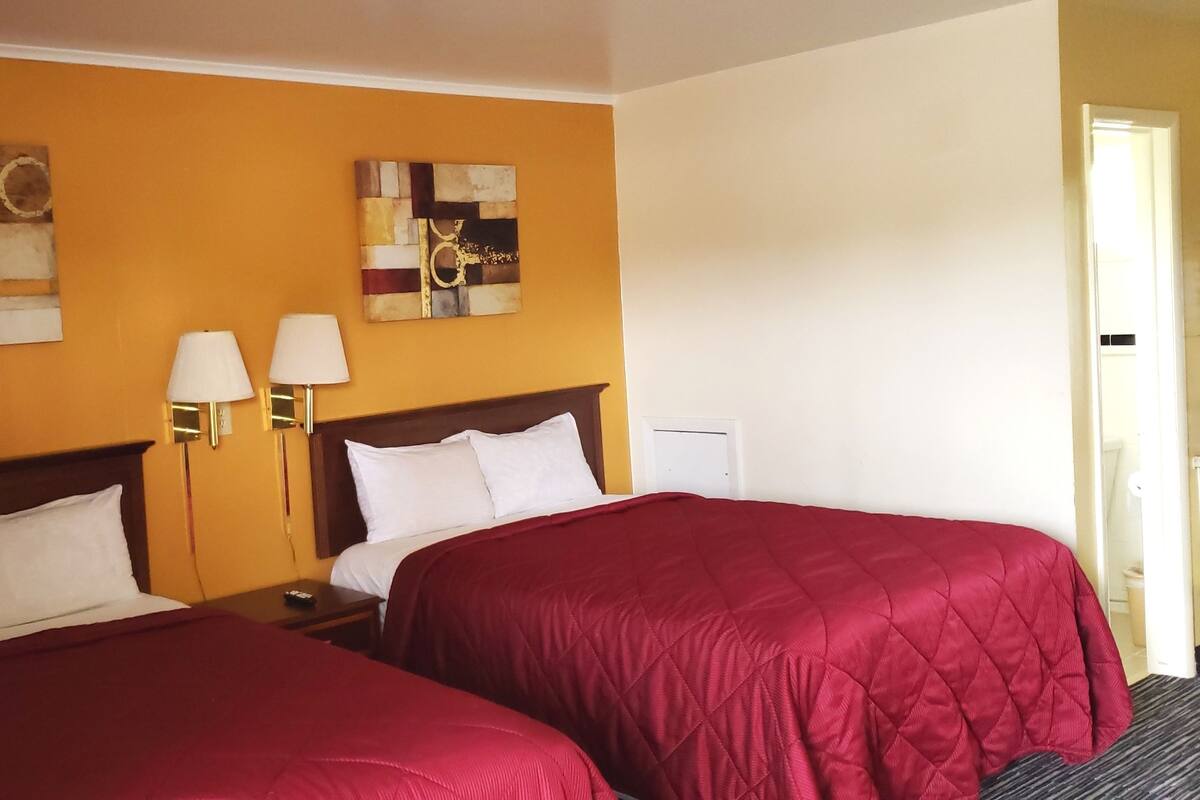 A hotel room with two beds, a wooden headboard, two bedside lamps, and two abstract wall art pieces.