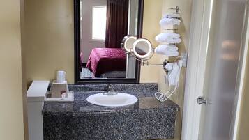 Un bagno d'albergo con un piano di lavoro in granito, un lavandino, uno specchio illuminato, un portasciugamani e una porta.