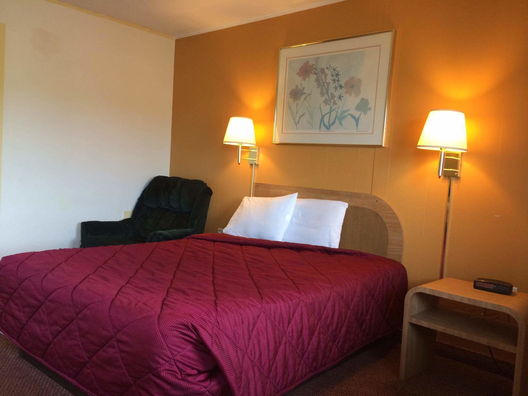A hotel room with a large bed, two bedside lamps, a chair, and a small table with a remote control.
