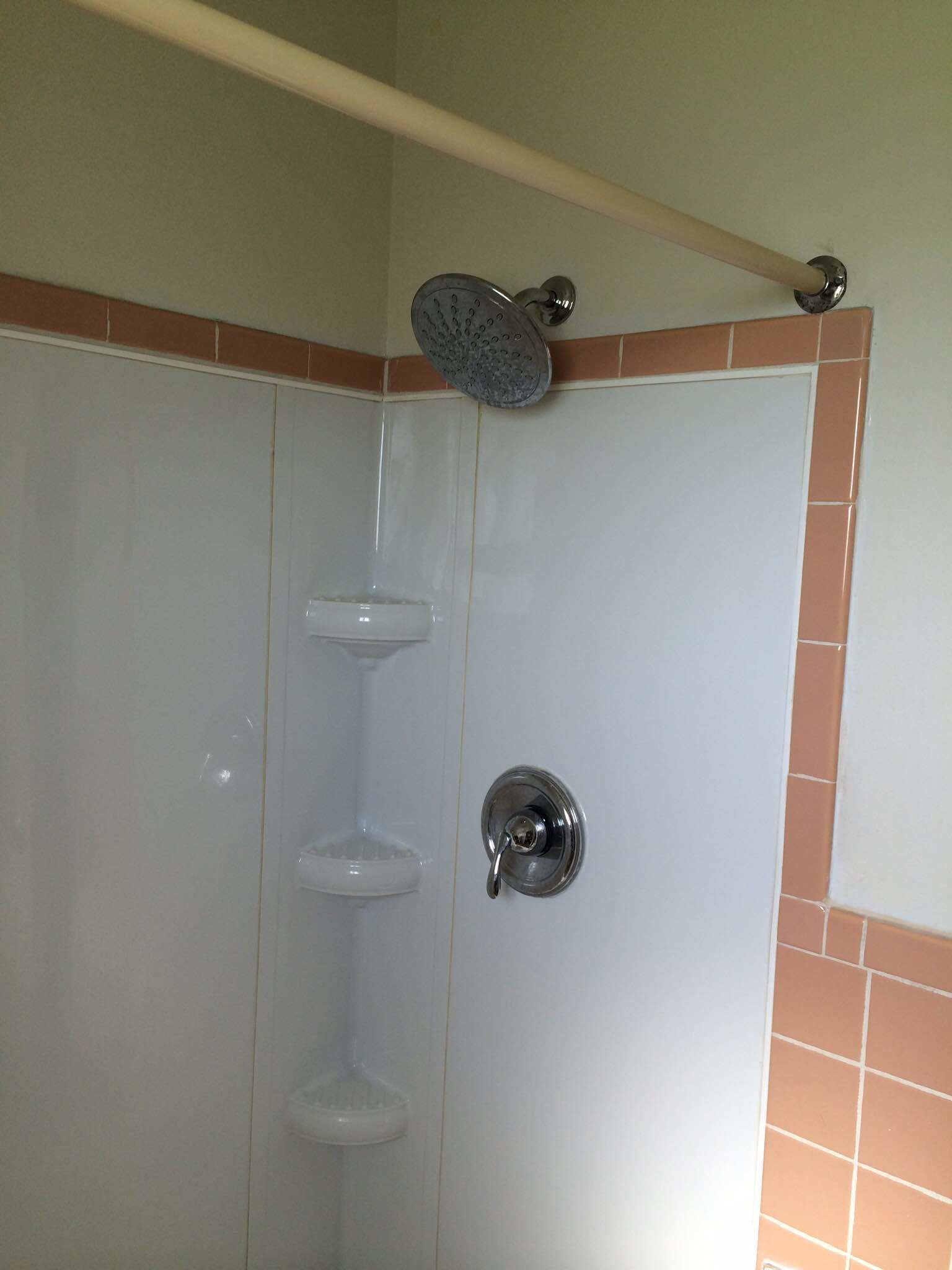 A shower with a handheld showerhead, a glass door, and a tiled wall.