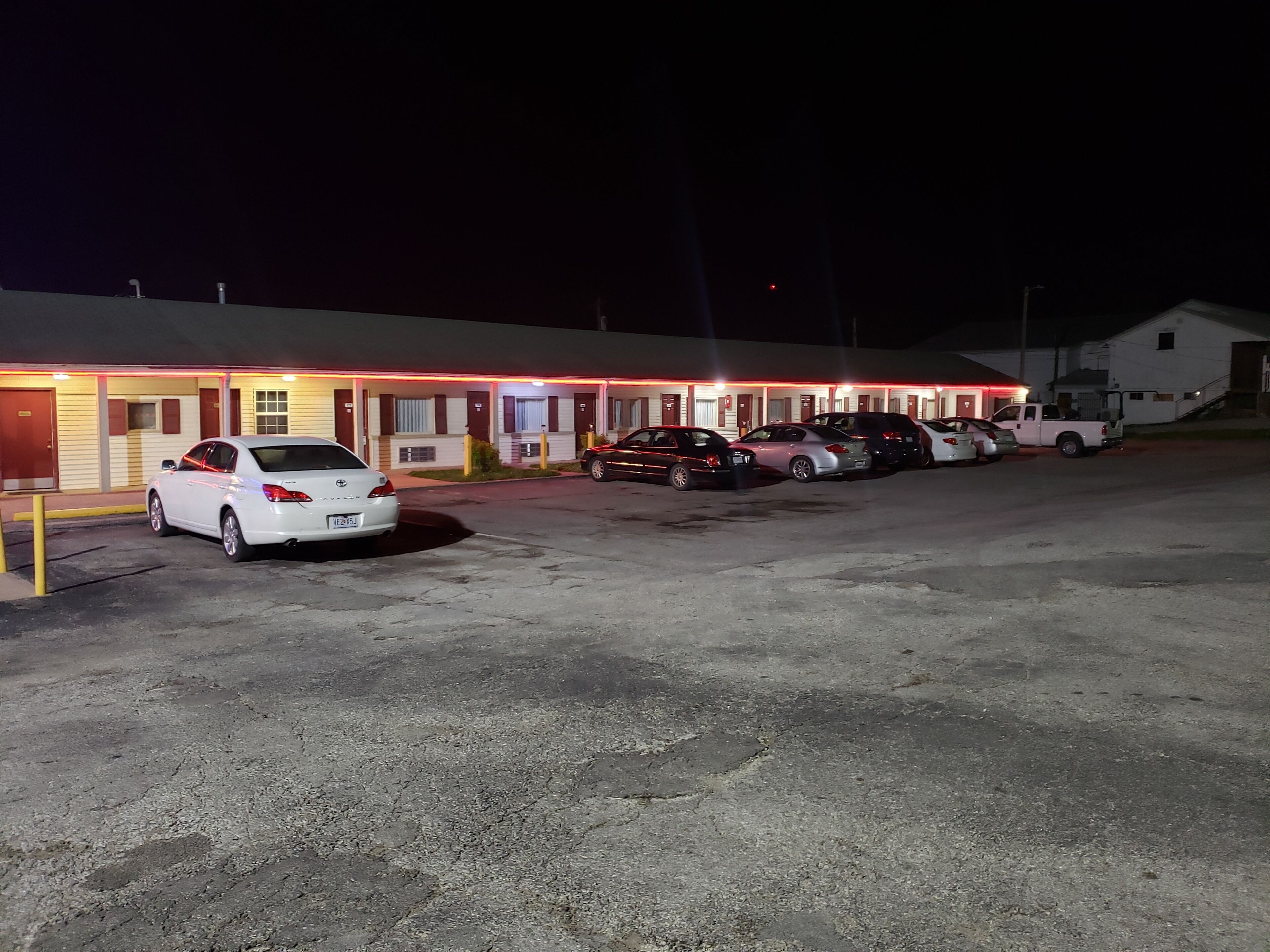 Um motel com vários quartos, um estacionamento e uma caminhonete branca estacionada na frente.