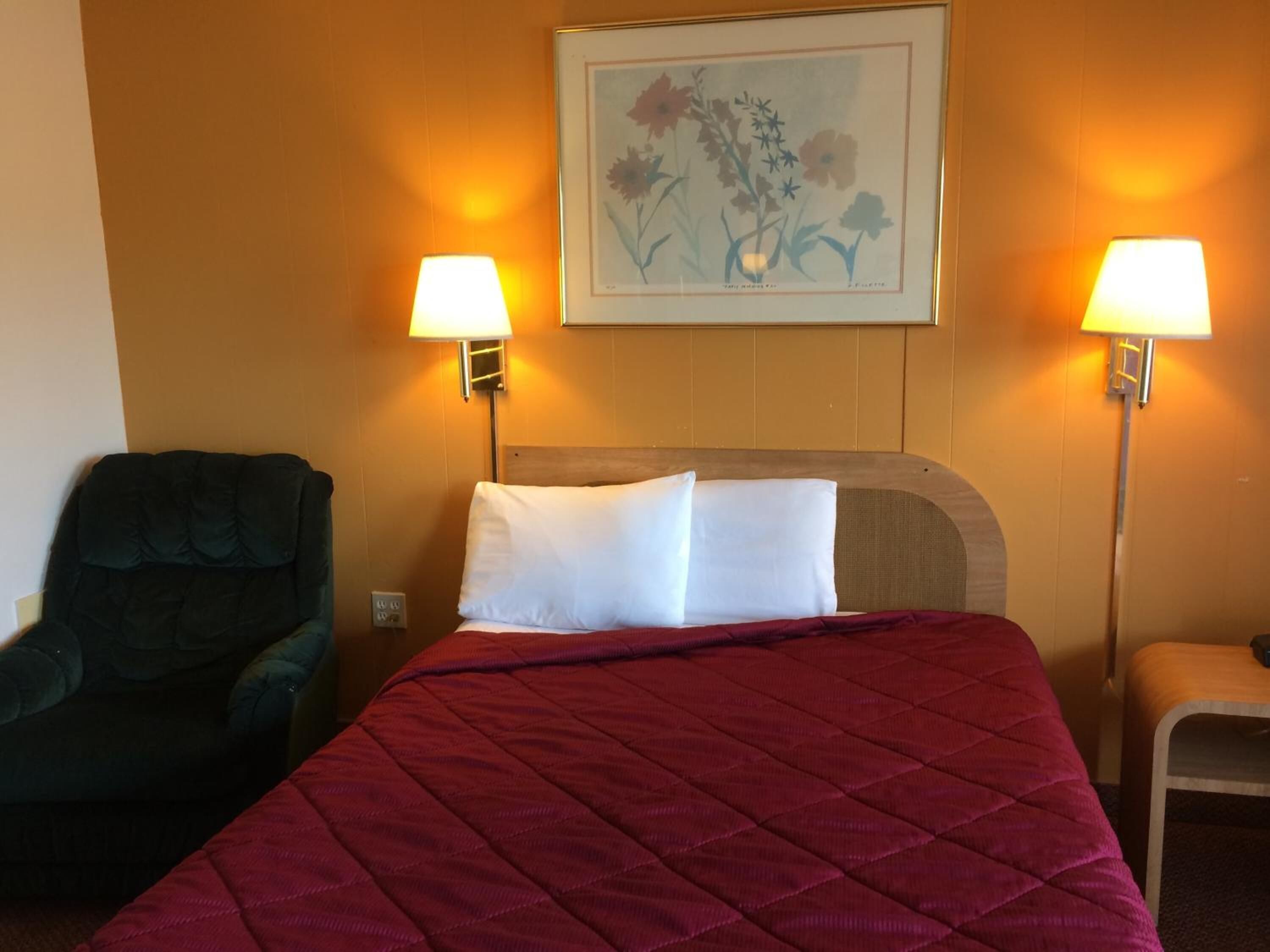 Una habitación de hotel con una cama, dos lámparas de pared, una silla y un cuadro.