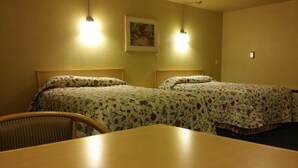 A hotel room with two beds, a wooden table, and a chair. - Budget Host Longhorn Motel (Byers)