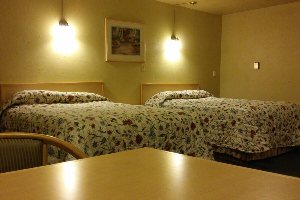 A hotel room with two beds, a wooden table, and a chair.