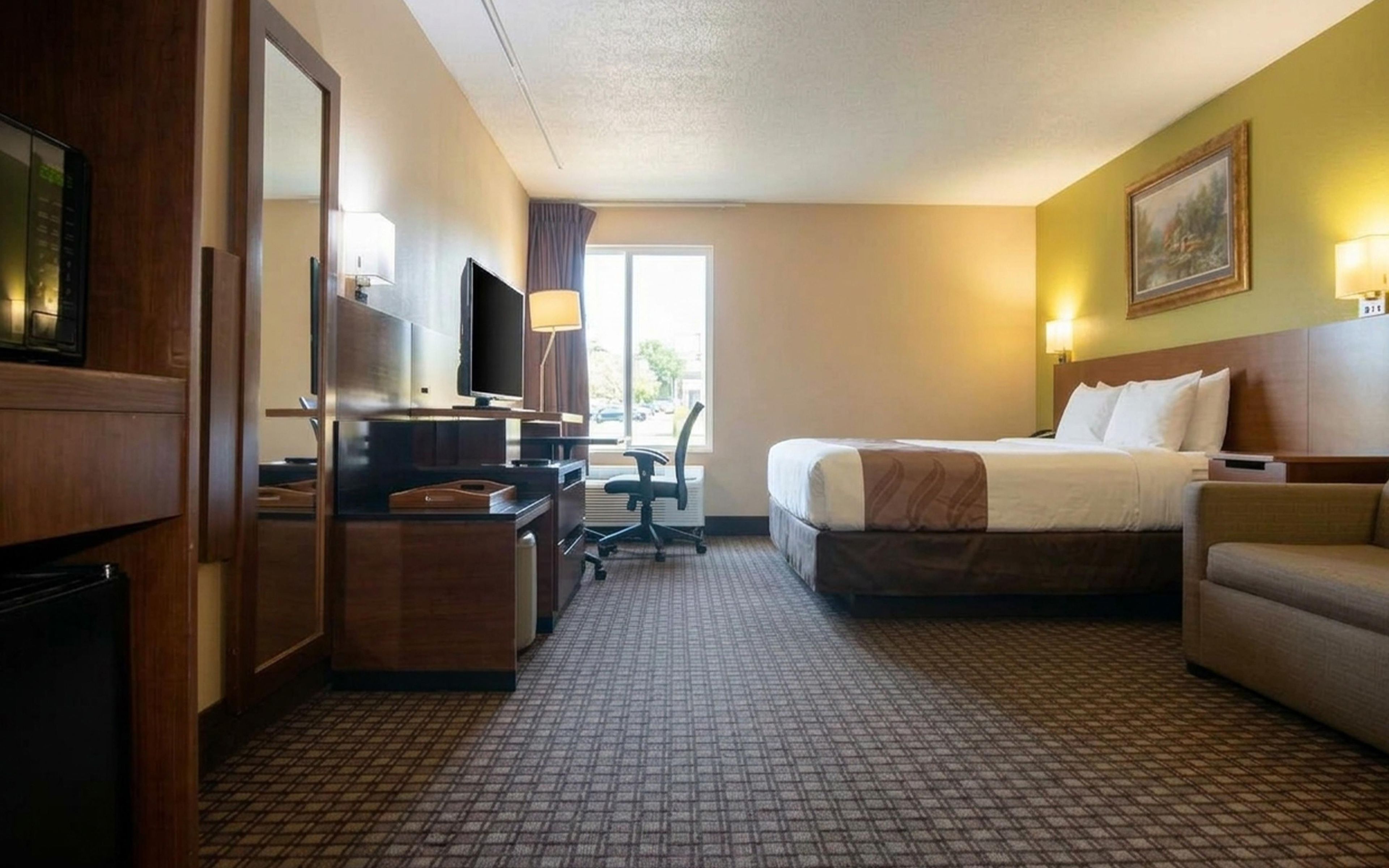 A hotel room with a bed, a desk with a computer, a chair, a television, and a window.
