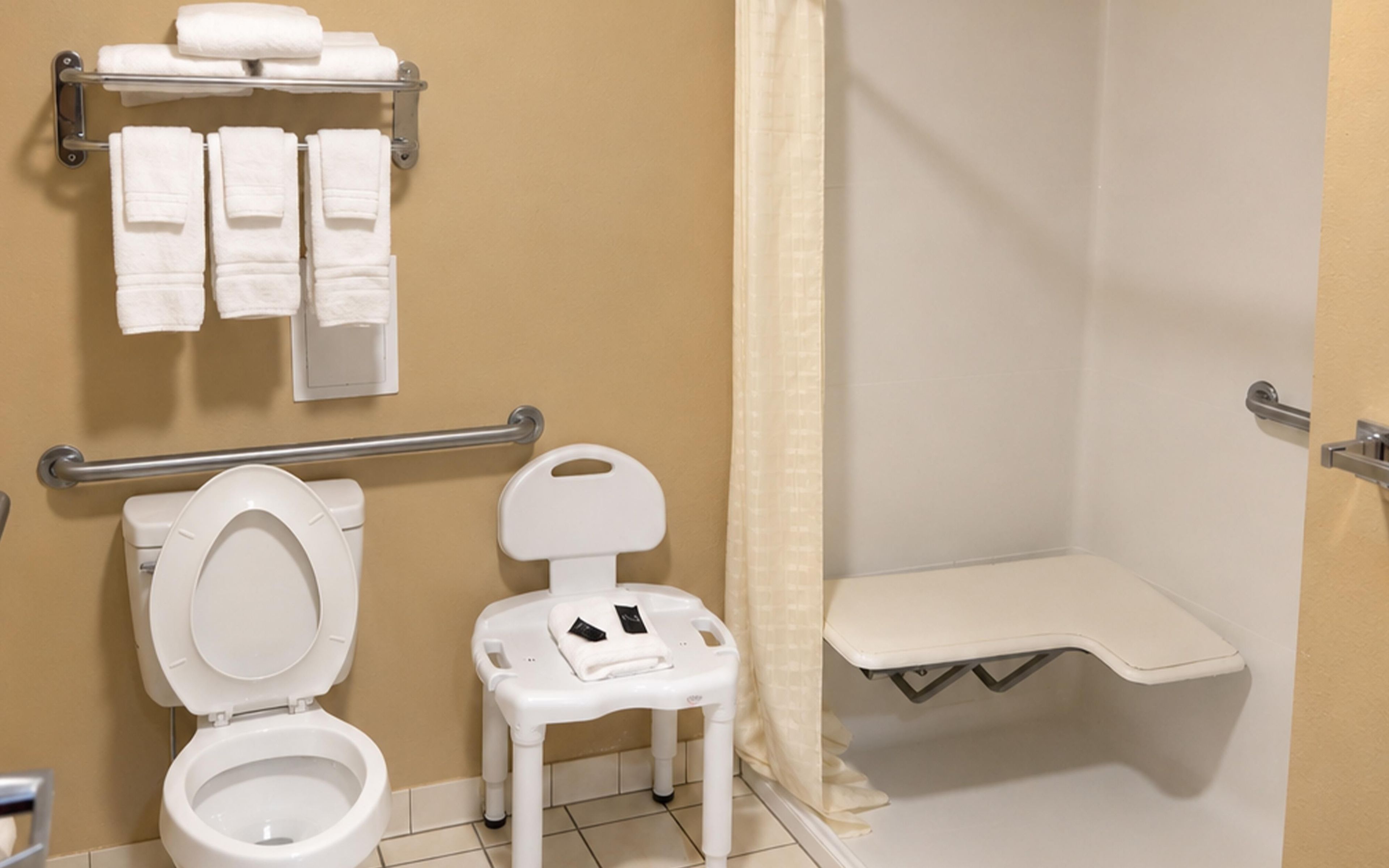 A bathroom with a toilet, a small white chair, a shower area, and a towel rack with multiple towels.