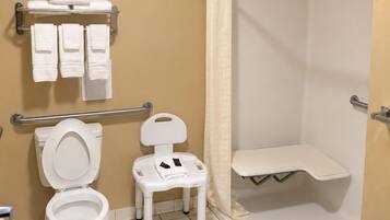 A bathroom with a toilet, a small white chair, a shower area, and a towel rack with multiple towels.